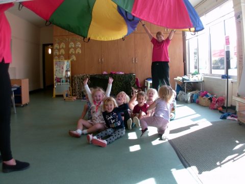 Children laughing whilst playing under a parachute